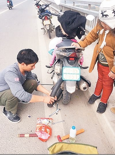 Thành viên đội bơm, vá xe miễn phí vá săm xe máy cho người đi đường trên cầu Nhật Tân.